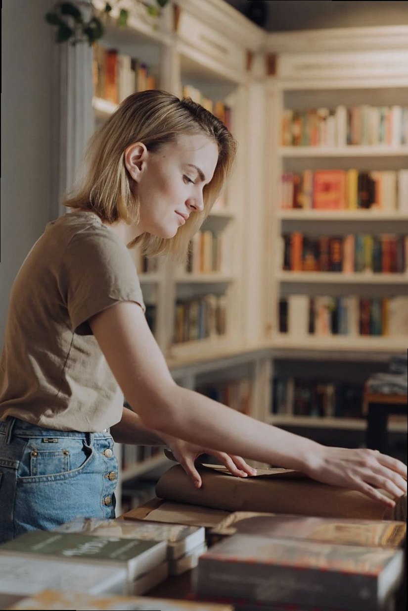 Jeune femme emballant des livres dans une librairie chaleureuse, illustrant un mélange de travail et de littérature.