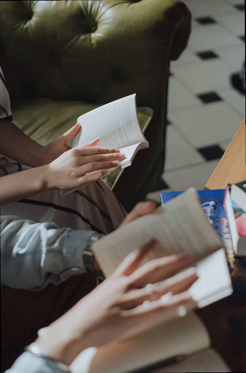 Mains tenant des livres dans une bibliothèque chaleureuse, idéal pour les thèmes de loisirs et d'éducation.
