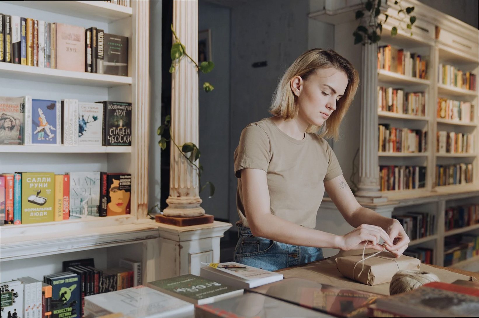 Jeune femme emballant des livres dans une librairie chaleureuse et accueillante, entourée d'étagères remplies de littéra